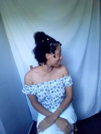 World Most beautiful lady Sher Trott Bailey showing off her amazing natural hair style in her off shoulder blouse and scratching her neck with a cute tendril with golden hair accessories. Sher had her hand in her lap and looking off to the side.