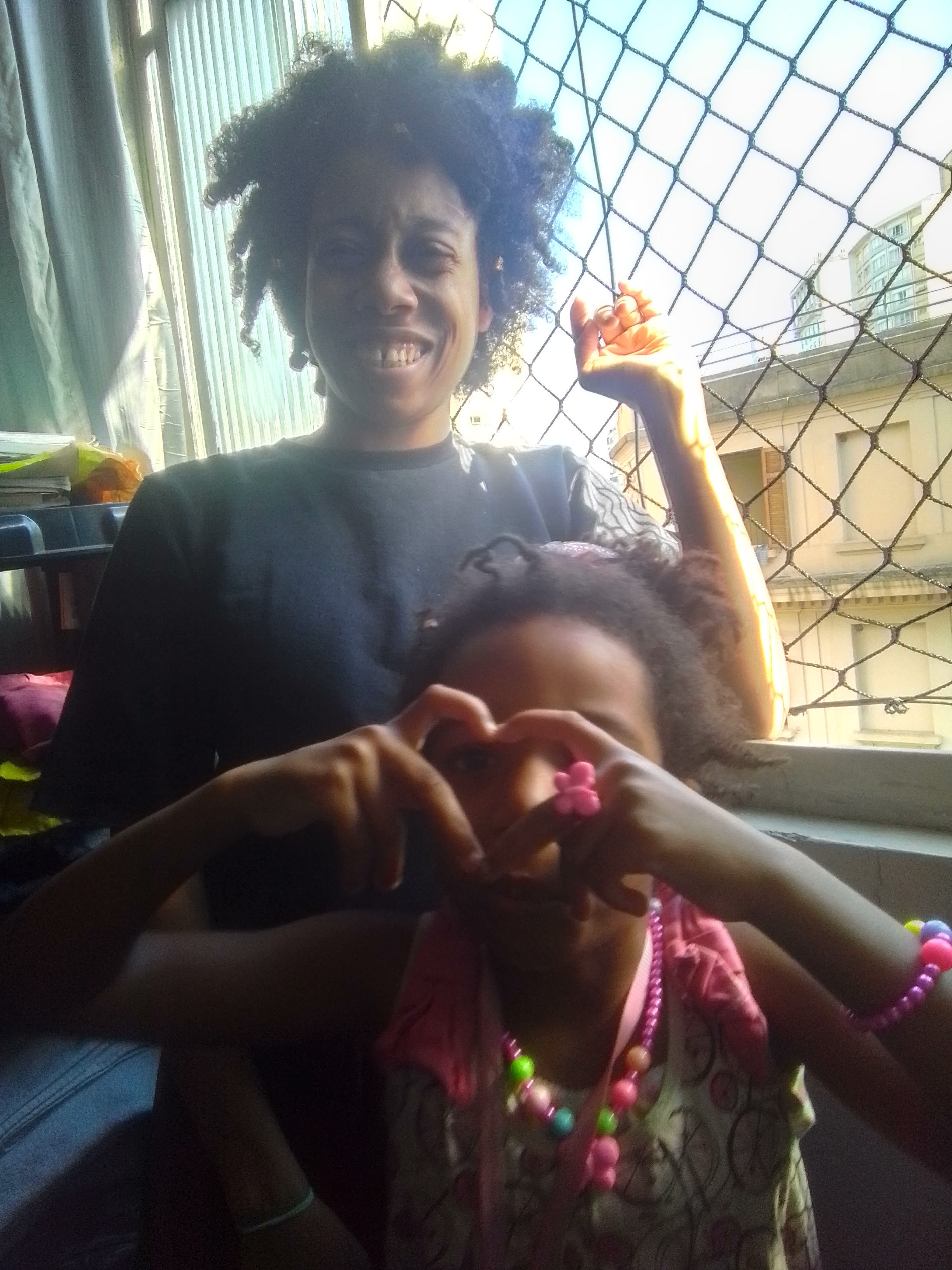 World Ruler Sher Trott Bailey and first princess Keilah Trott Bailey take a photo together and Keilah uses her fingers to make a heart over her face while mom stands at the window at our roach hotel in Sao Paulo