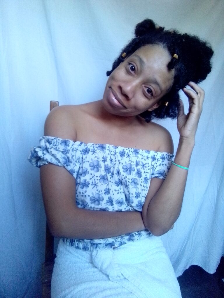 World Most beautiful lady Sher Trott Bailey showing off her amazing natural hair style in her off shoulder blouse and scratching her neck with a cute tendril with golden hair accessories. Sher had her hand in her lap and looking off to the side.
